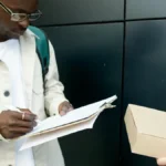 Kurir pengiriman menandatangani dokumen serah terima paket di luar ruangan, menggambarkan proses pengiriman barang dengan surat order